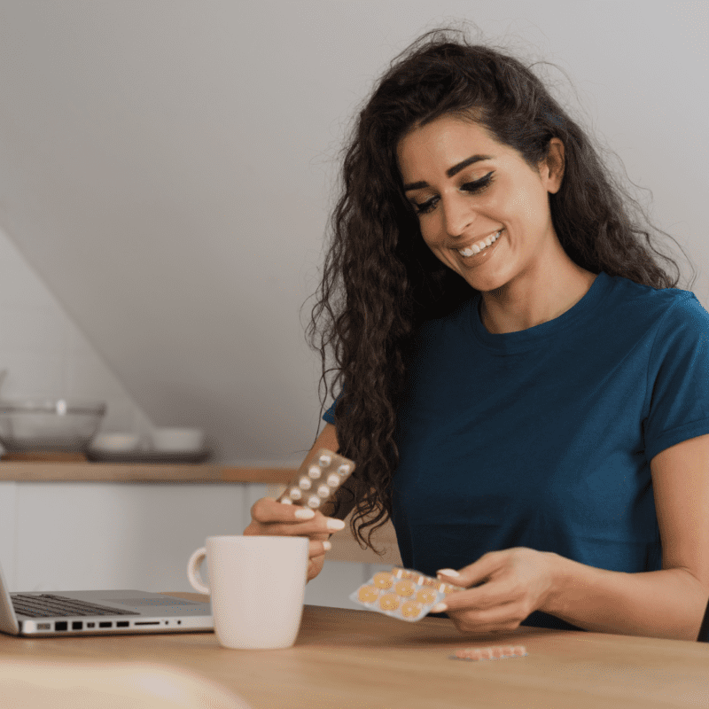 Mujer con su laptop y suplementos en la mesa.