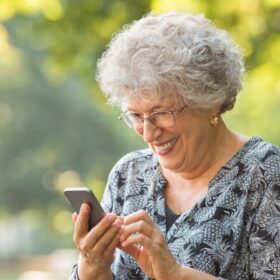 Mujer mayor sonriendo mientras usa su teléfono móvil